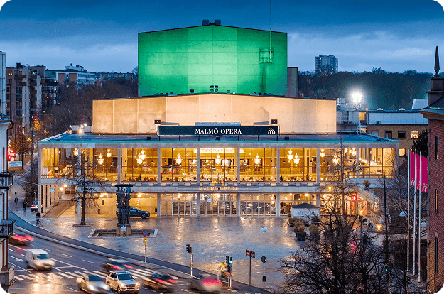 Malmö Opera building at dusk with a green-lit roof and illuminated facade.