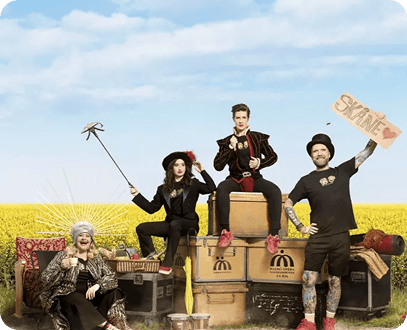 Four unique people pose on luggage in a vibrant yellow field; one holds a "SKANE" sign.